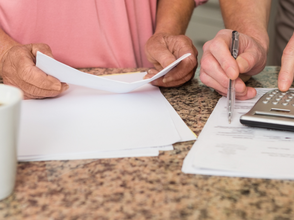 Two people looking at monthly bill, all that is shown is their torsos and hands and paper and a calculator and a cup of coffee.