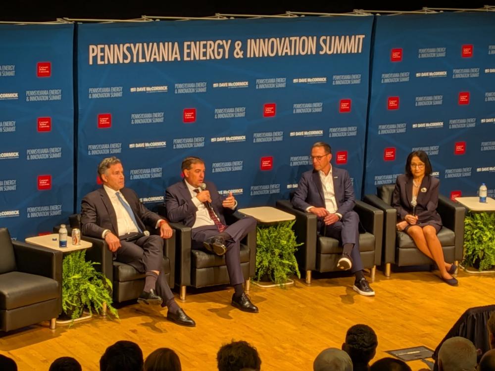Panel of 4 people in business attire sitting on stage in front of a Pennsylvania Energy & Innovation Summit backdrop 